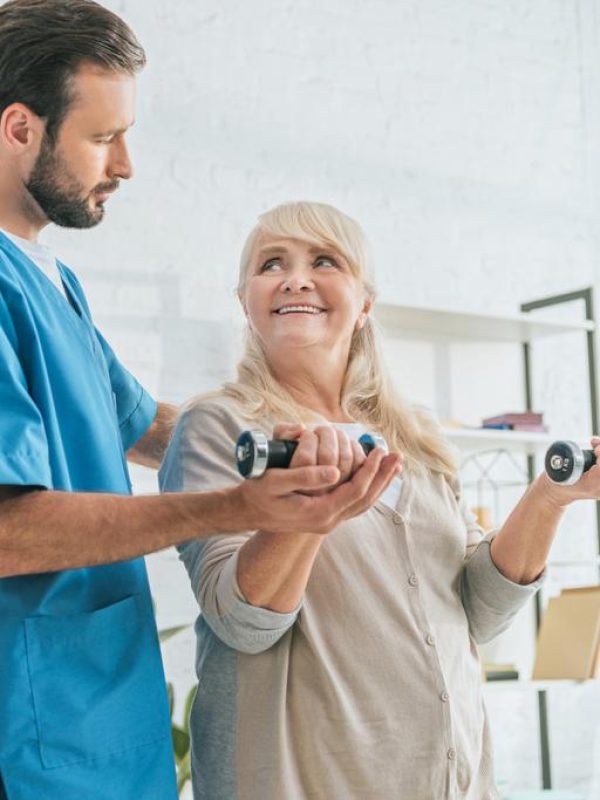 stock-photo-social-worker-looking-smiling-senior-woman-exercising-dumbbells